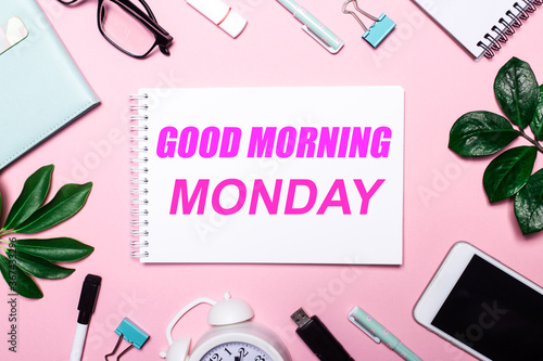 Good morning monday written on pink background near stationery and green leaves. Motivational Concept
