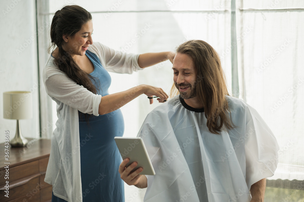 The pregnant woman is cutting her husband. Bearded man getting haircut by his wife at home new normal concept. The pregnant woman is cutting her husband. Bearded man getting haircut by his wife at home new normal concept.