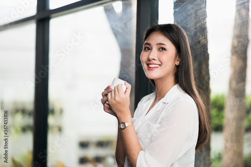 Beautiful asian woman drinking coffee at home in the morning. Smiling charming happy young female stay at home.