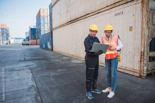 Two foreman man & woman worker working checking at Container cargo harbor holding laptop computer and using walkie-talkie to loading containers.