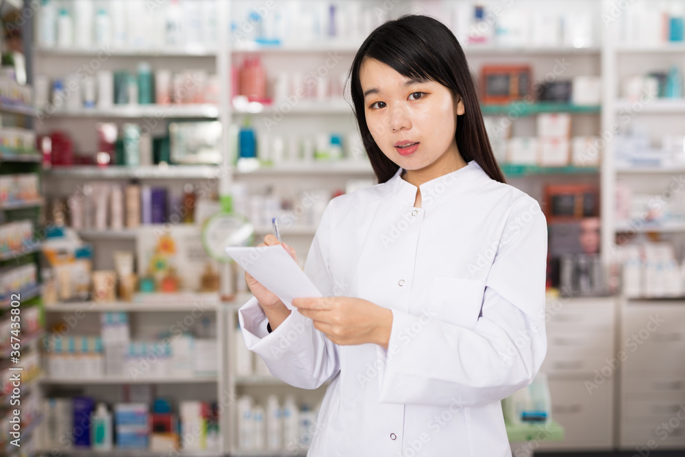 Chinese female is checking medicine with notebook in pharmacy