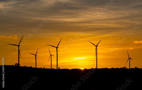 Silhouette wind turbine with twilight sky and sunlight ray for clean energy plant on the mountain.