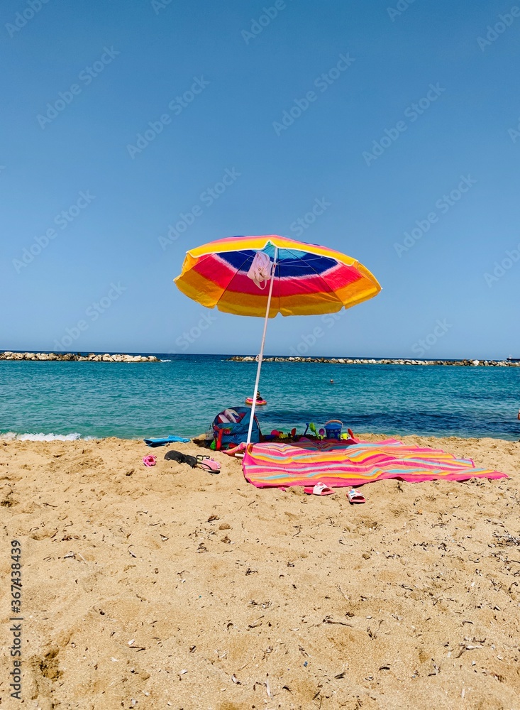 Colourful parasol on the beach. Single umbrella and towel on empty sandy beach and beautiful water of Mediterranean sea. Colourful parasol on the beach. Single umbrella and towel on empty sandy beach and beautiful water of Mediterranean sea.