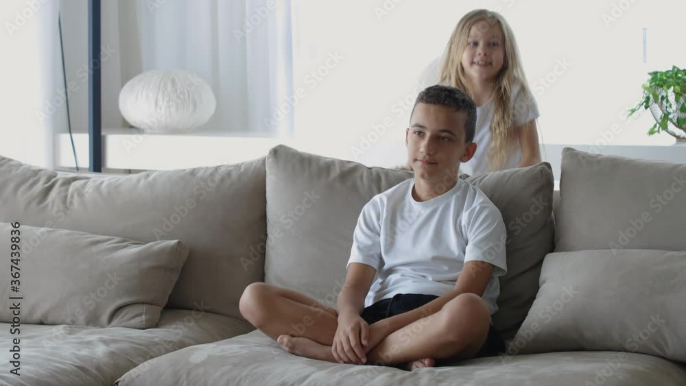 Caucasian little sister and brother in white T-shirts and blond hair sitting at the table. sister hugs brother Caucasian little sister and brother in white T-shirts and blond hair sitting at the table. sister hugs brother