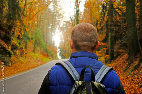 Autumn travel. Tourism and hiking in the autumn. A man with a backpack on the road with autumn trees in the sunshine.Autumn landscape. Fall season.view of road with trees on a sunny day