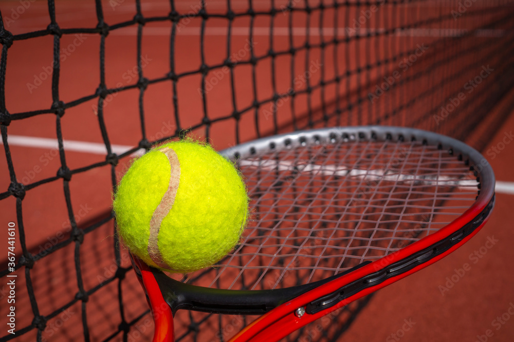 Tennis ball on a racket alongside a net
