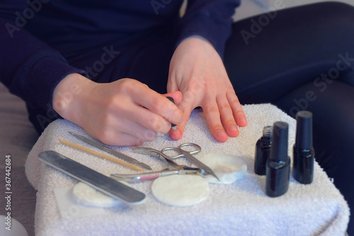 Woman is applying primer using brush on nails before cover it shellac gel polish, hands closeup. Girl making manicure at home for herself sitting on sofa. Hygiene care about nails. Beauty procedure.