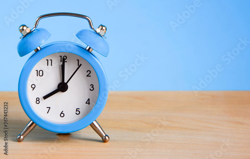 Blue alarm clock on wooden table and blue background close up with space for text, copy space. 8 a.m. Time concept. Breakfast concept.