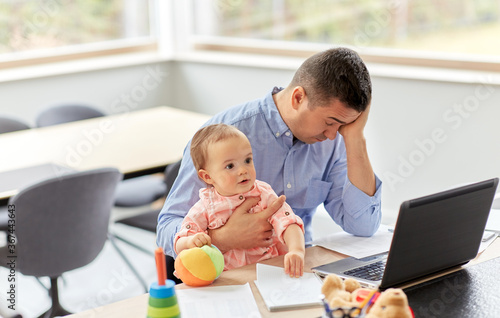 remote job, multi-tasking and family concept - tired middle-aged father with baby working on laptop at home office