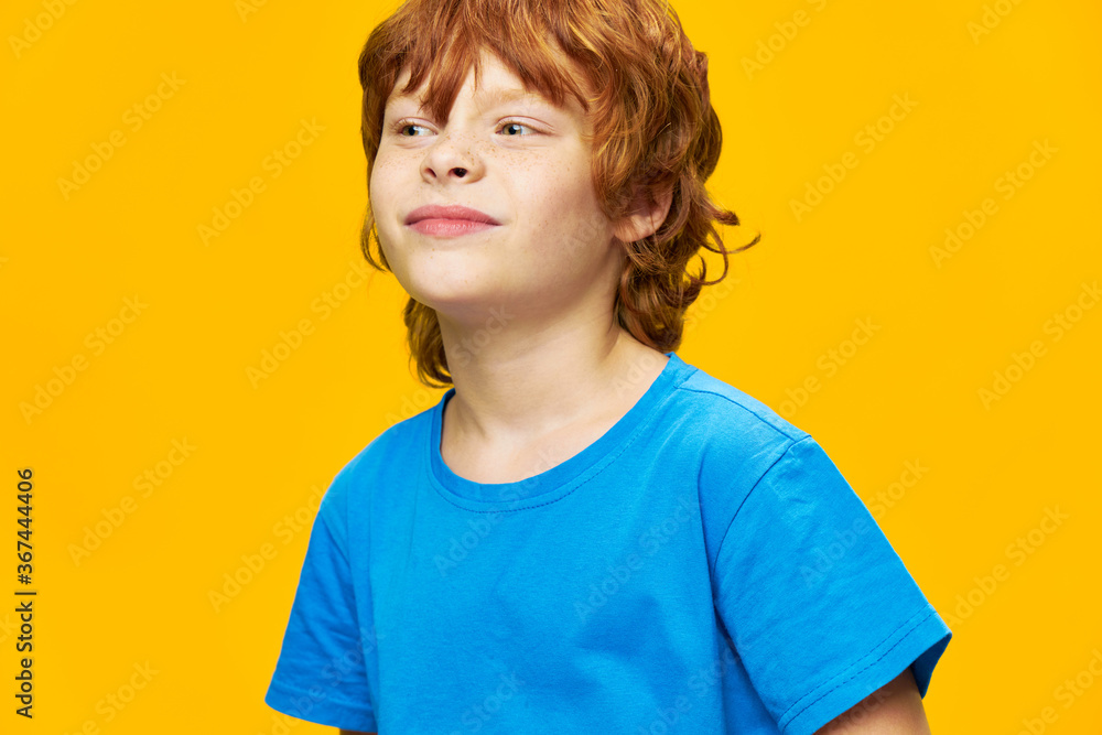 The boy looks away blue t-shirt yellow background red hair The boy looks away blue t-shirt yellow background red hair