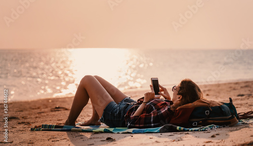 Happy young woman resting lying on a smartphone in the hands at sunset on the beach