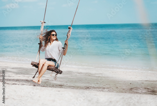 Young beautiful curly woman girl swinging and having fun on a swing on a tropical beach vacation and travel concept.