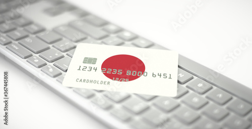 Plastic bank card depicting flag of Japan on computer keyboard. Fictional numbers photo