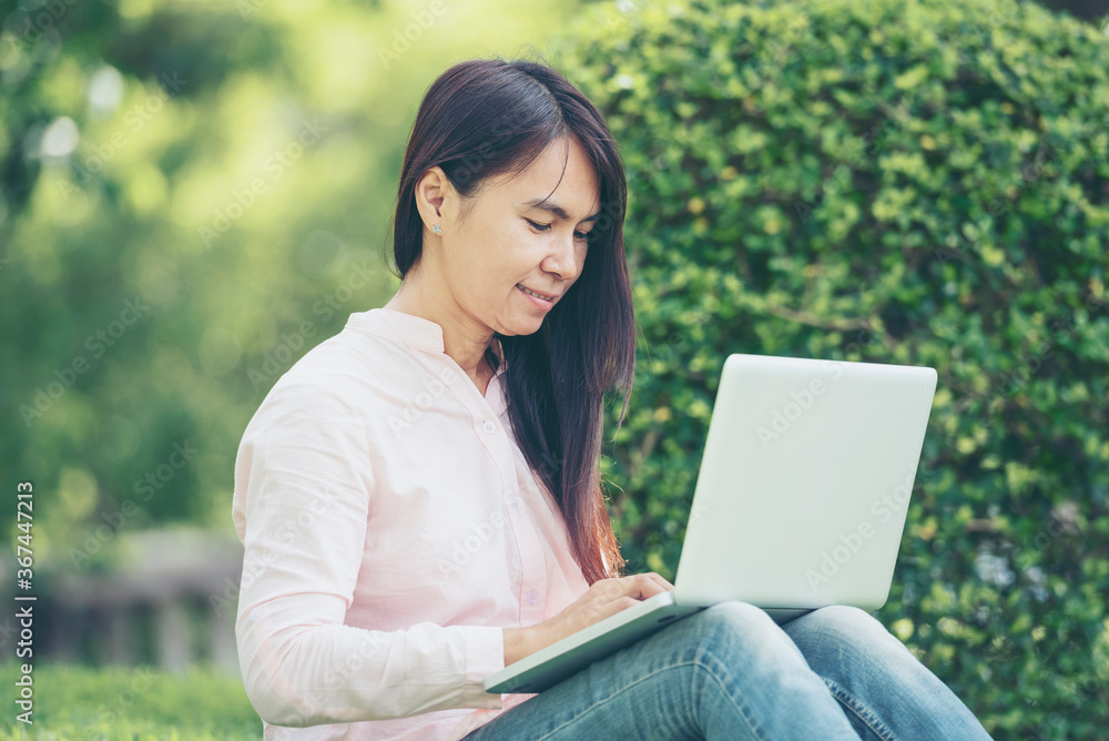 Asian woman sitting green park using laptop computer. Woman working on laptop happy entrepreneur business using notebook with hands typing on keyboard home office during coronavirus quarantine period Asian woman sitting green park using laptop computer. Woman working on laptop happy entrepreneur business using notebook with hands typing on keyboard home office during coronavirus quarantine period