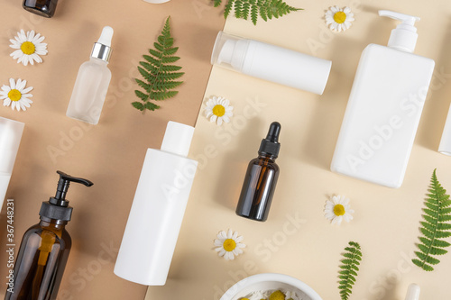 Set of care cosmetics. Various bottles, tubes with cosmetic, chamomile flowers, fern leaves on a beige and brown background. Beauty concept. Top view Flat lay