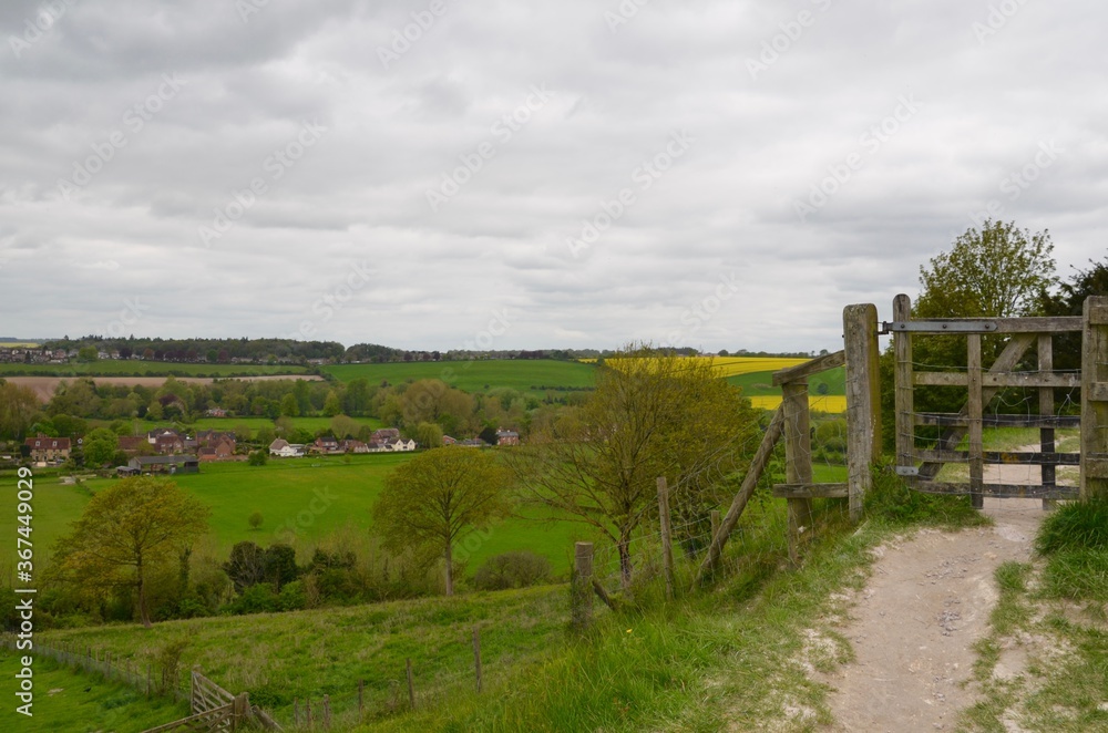 Wooden gate on path with panoramic views of countryside in Salisbury, England. Views of green and yellow fields and villages
