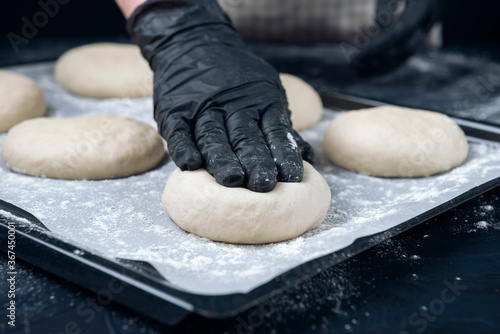 Woman in checkered apron and black gloves are pushing a piece of yeast dough. Process of making bakery. Adjarian Khachapuri Recipe – Georgian cheese bread.