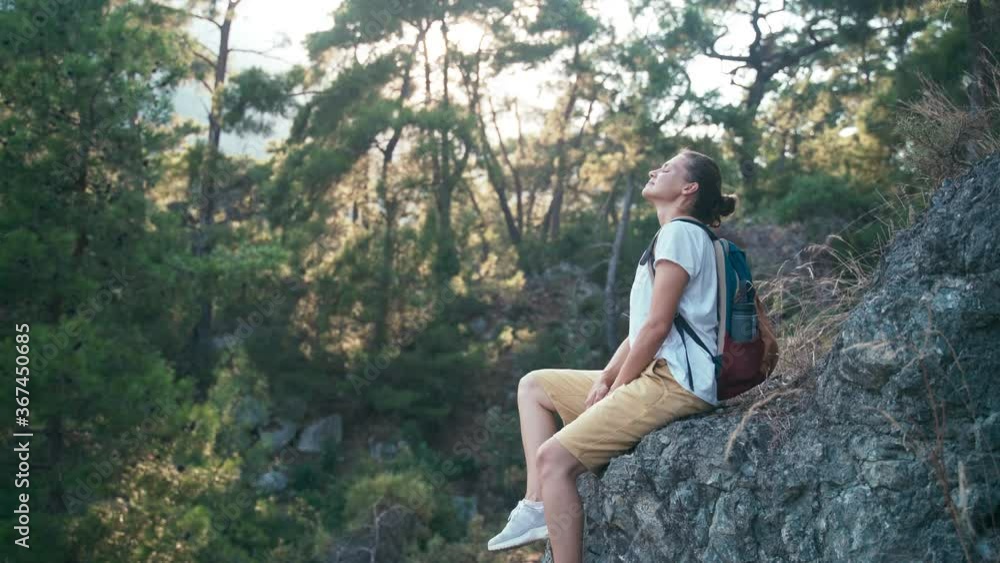 Young woman traveler with a backpack sitting on a rocky mountainside and enjoying fresh mountain air while resting. Young woman traveler with a backpack sitting on a rocky mountainside and enjoying fresh mountain air while resting.