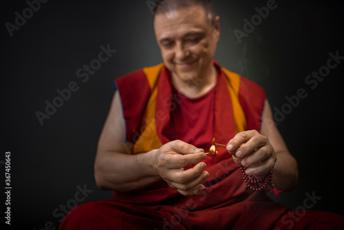 Valokuvatapetti Buddhist monk in red kesa, holding an incense stick with incense in his hand