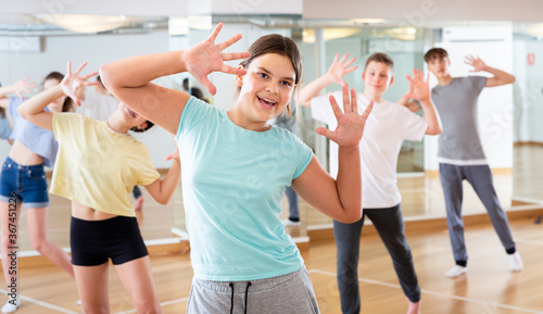 Fototapeta Naklejka Na Ścianę i Meble -  Portrait of emotional teenager girl doing dance workout during group class in studio