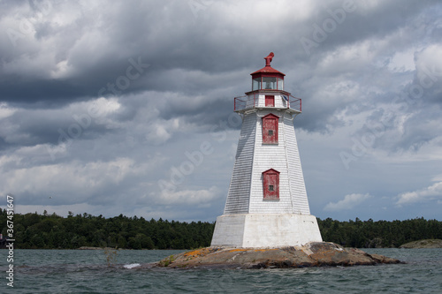 Light house in the middle of a lake near the Sault Ste. Marie coast. The skies are cloudy and dramatic. The light house is white and red.