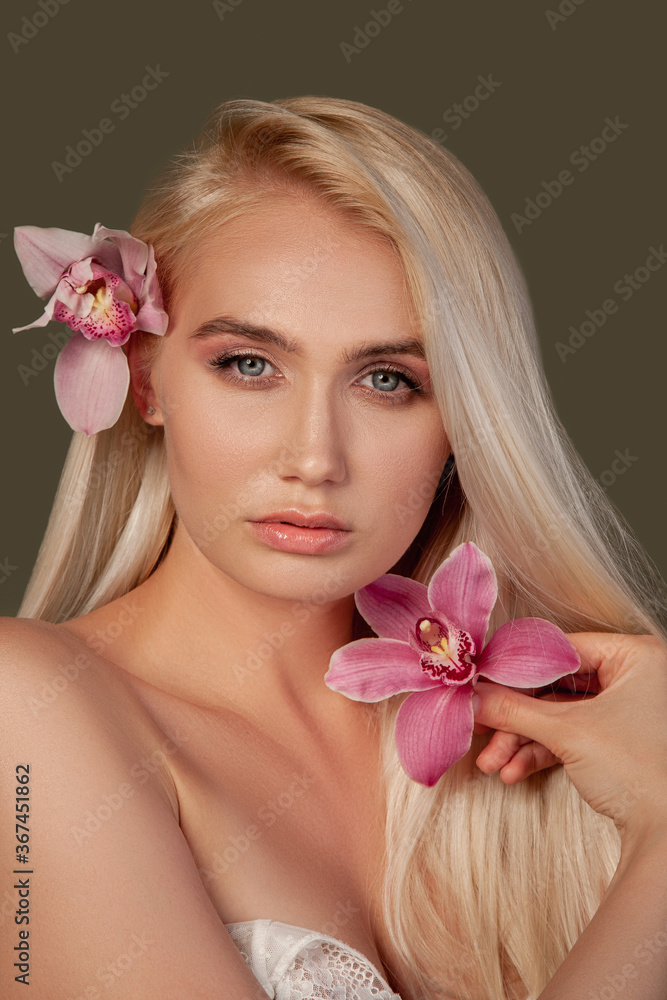 Beauty face. Spa therapy. Blonde woman with natural makeup perfect skin orchid flowers isolated on brown.