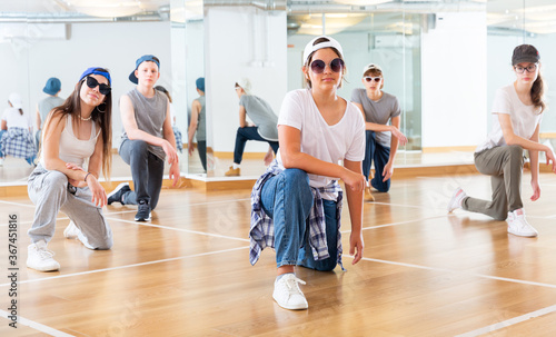 Positive teen girls and boys posing on knees in dance studio during hip hop class