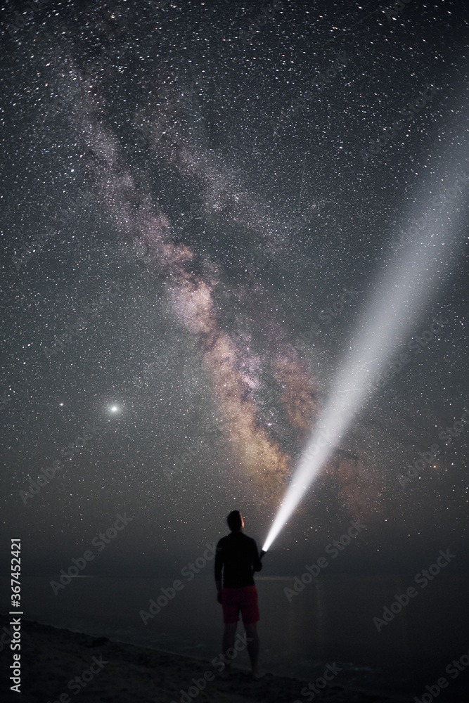 traveller and galaxy. milky way astrophoto. man stands on the sea shore with flash light. light beam and man during night.