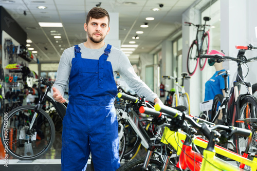 Portrait of young cheerful repairman standing near cycle in bicycle store