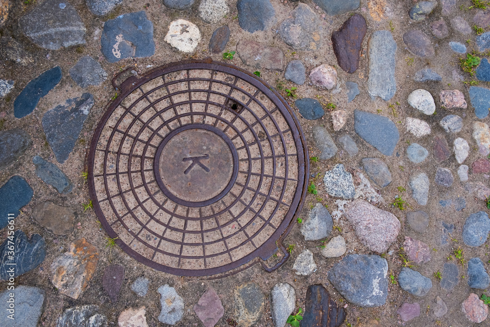 A manhole cover on an old cobblestone pavement