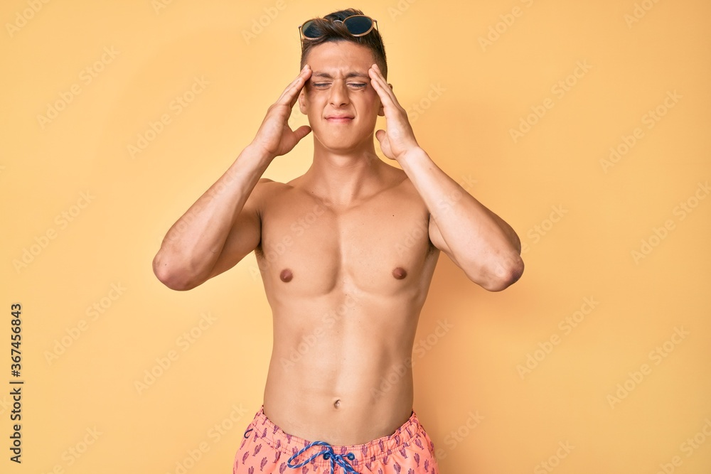 Young hispanic boy wearing swimwear shirtless suffering from headache desperate and stressed because pain and migraine. hands on head.