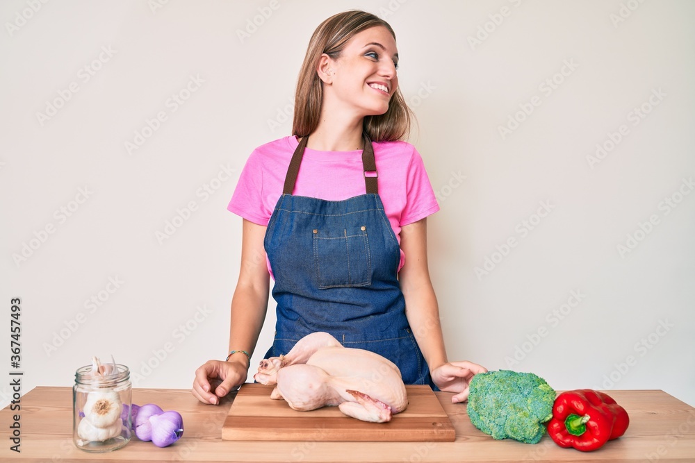 Young blonde girl wearing cook apron and holding chicken looking away to side with smile on face, natural expression. laughing confident. Young blonde girl wearing cook apron and holding chicken looking away to side with smile on face, natural expression. laughing confident.