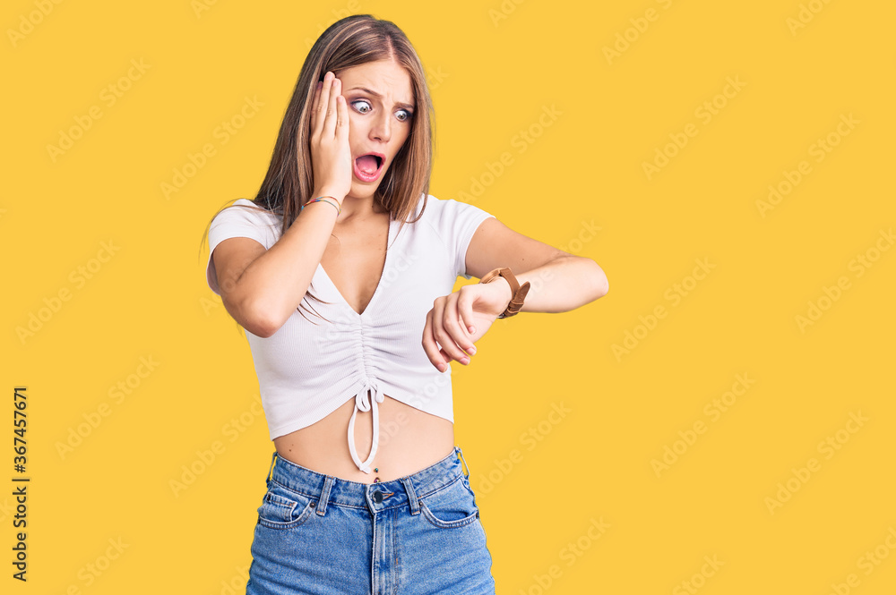 Young beautiful blonde woman wearing casual white tshirt looking at the watch time worried, afraid of getting late Young beautiful blonde woman wearing casual white tshirt looking at the watch time worried, afraid of getting late