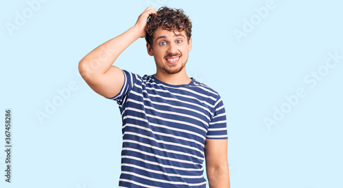 Young handsome man with curly hair wearing casual clothes confuse and wonder about question. uncertain with doubt, thinking with hand on head. pensive concept.