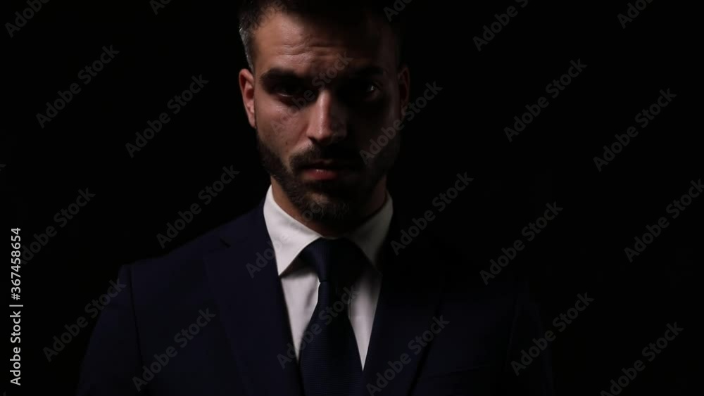 sexy young businessman in suit looking up and down, fixing suit and tie, moving and holding hands to face and touching beard and chin, thinking and walking away in the dark sexy young businessman in suit looking up and down, fixing suit and tie, moving and holding hands to face and touching beard and chin, thinking and walking away in the dark