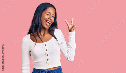 Young indian girl wearing casual clothes smiling with happy face winking at the camera doing victory sign. number two.