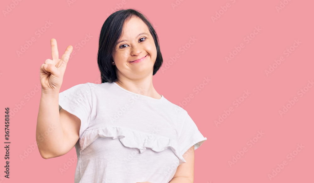 Brunette woman with down syndrome wearing casual white tshirt smiling looking to the camera showing fingers doing victory sign. number two. Brunette woman with down syndrome wearing casual white tshirt smiling looking to the camera showing fingers doing victory sign. number two.