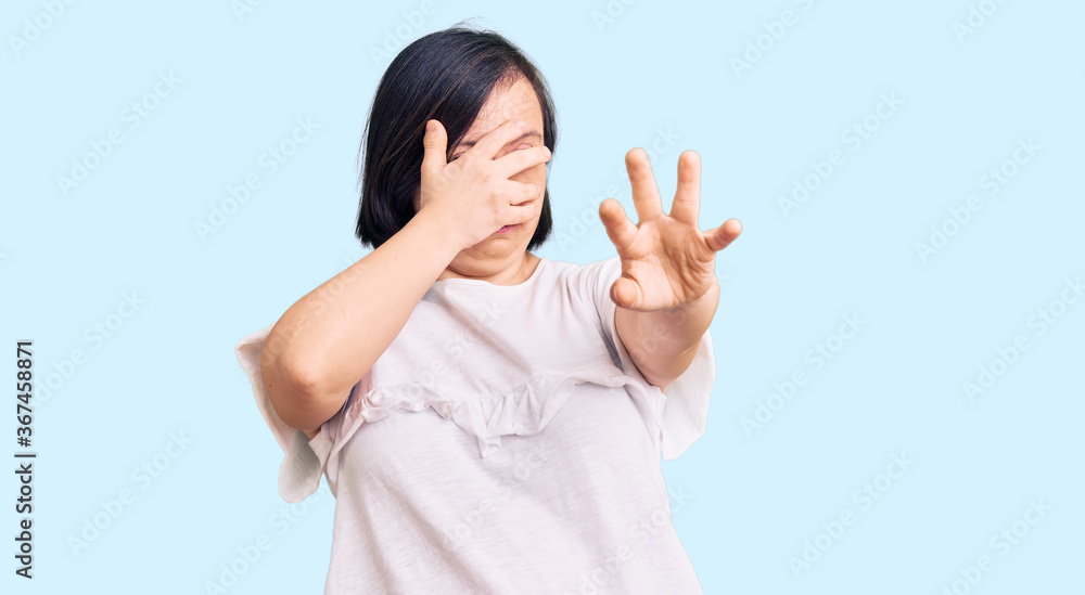 Brunette woman with down syndrome wearing casual white tshirt covering eyes with hands and doing stop gesture with sad and fear expression. embarrassed and negative concept. Brunette woman with down syndrome wearing casual white tshirt covering eyes with hands and doing stop gesture with sad and fear expression. embarrassed and negative concept.