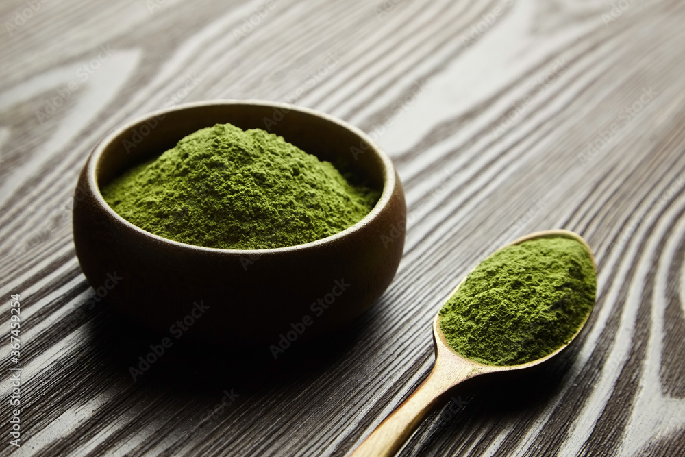 Freeze dried wheatgrass powder in spoon and bowl on dark wooden background. Freeze dried wheatgrass powder in spoon and bowl on dark wooden background.