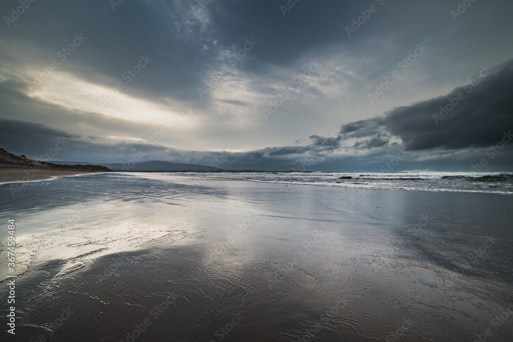 Strandhill Beach with low clouds on rough sea as the sun sets. Cloudy sunset on Strandhill with deep gray and blue color spectrum conveys deep thoughts and melancholic concept - County Sligo, Ireland