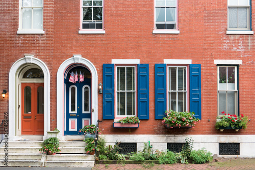 Red brick wall with blue window shutters and blue door. Colonial age brick building with plants on front steps. Historical building in Philadelphia United States.