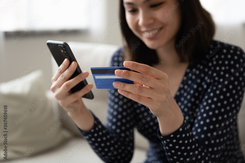 Crop close up of happy Asian millennial girl hold plastic credit card make payment or purchase on cellphone from home, smiling young Vietnamese woman shopping on internet using smartphone - obrazy, fototapety, plakaty 