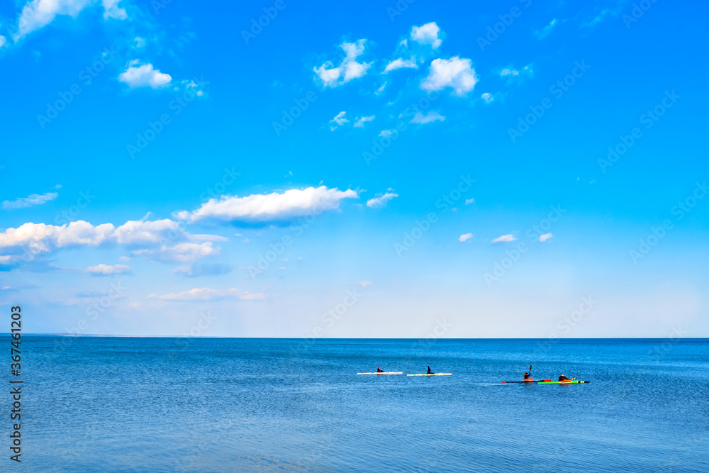 A company of young people on kayaks is training at sea. Four multi-colored canoes sail in the blue sea. Spring canoe training in the open sea on the background of a beautiful sky with clouds.