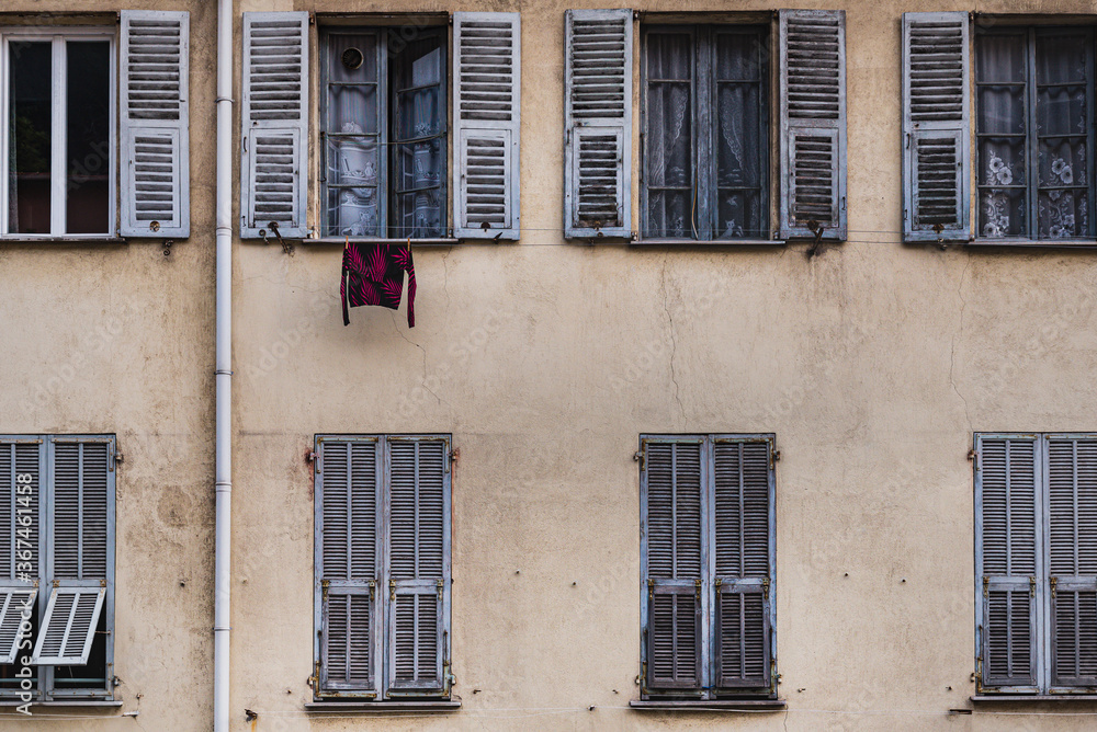 Hanging shirt at a window on a traditional old French facade with rows of open and closed louvered shutters (jalousie) conveys a downtown lifestyle and privacy, living together concept - Nice, France