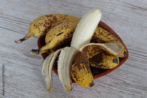 Bananas with speckleses and dark stains on their skin in wooden bowl close up top view photo