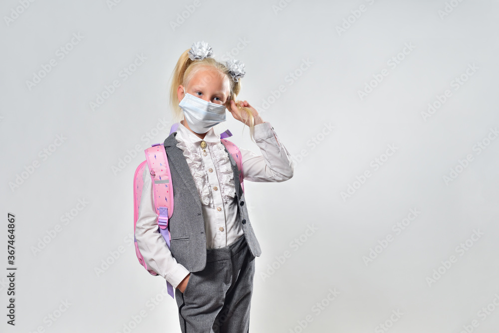 Schoolgirl with a backpack and a protective mask on a gray background with copy space Schoolgirl with a backpack and a protective mask on a gray background with copy space