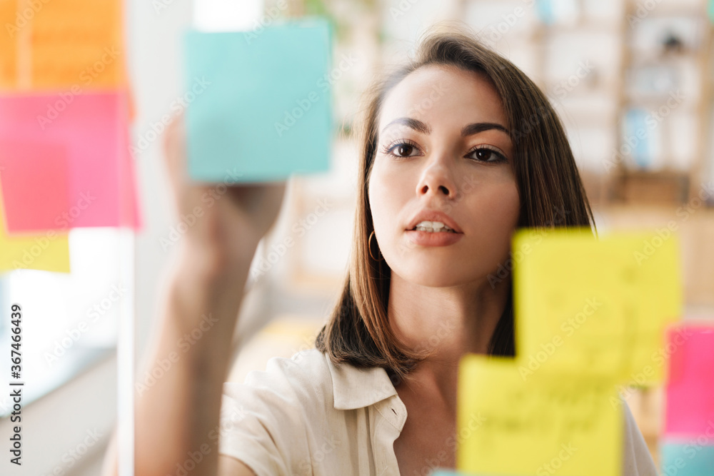 Image of young beautiful serious woman using marker pen and stickers Image of young beautiful serious woman using marker pen and stickers