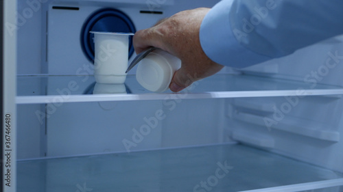 Hungry Man Opens the Refrigerator Door Looking for Food Inside, Takes a Fresh and Cold Yogurt and a Teaspoon © EuStock