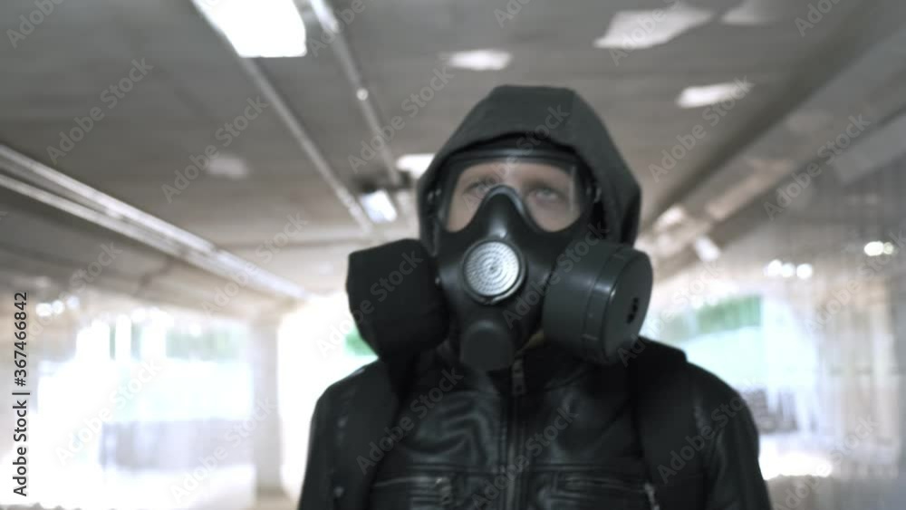 man in gas mask, black jacket with hood walking through long tunnel, underpass. protection from chemical weapons, virus epidemic. Post apocalyptic world. survivor, stalker after nuclear, chemical war man in gas mask, black jacket with hood walking through long tunnel, underpass. protection from chemical weapons, virus epidemic. Post apocalyptic world. survivor, stalker after nuclear, chemical war