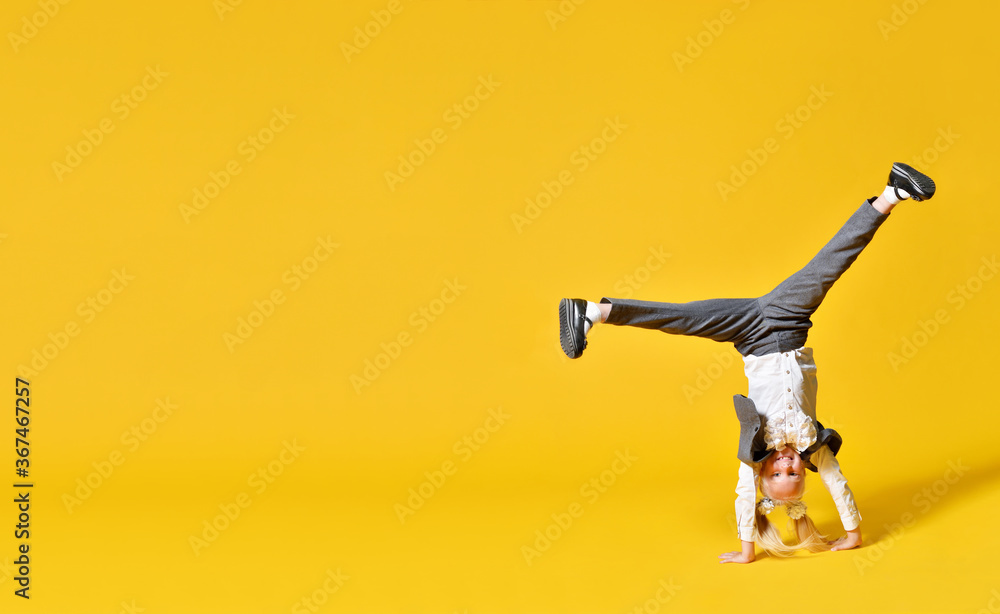 Active happy girl child upside down on yellow background